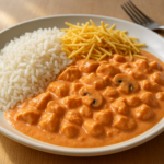 Prato de estrogonofe de frango cremoso servido com arroz branco e batata palha em mesa de almoço caseiro.